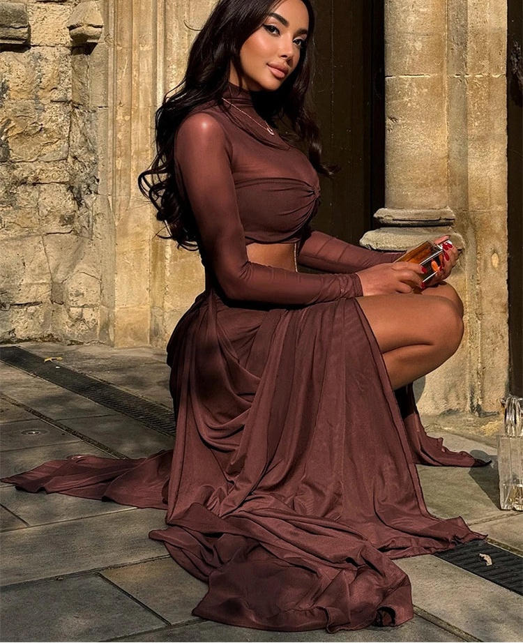 Woman in a long brown dress sitting on a stone floor with a stone building in the background.