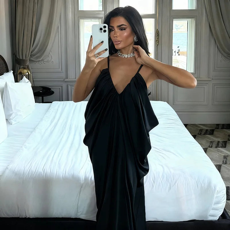 Woman in a black dress taking a mirror selfie in a bedroom.
