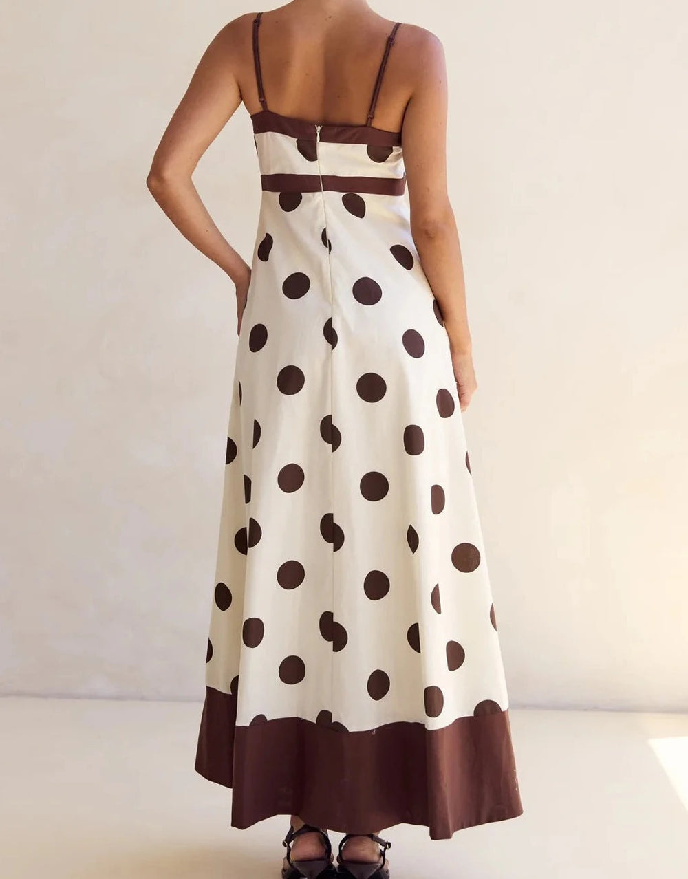 Woman wearing a polka dot dress with brown and white pattern on a plain background