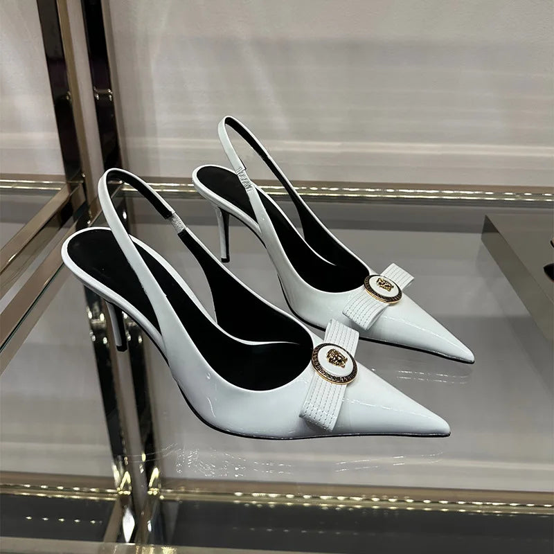 Pair of white pointed toe slingback heels with a bow detail and gold metal accent on display