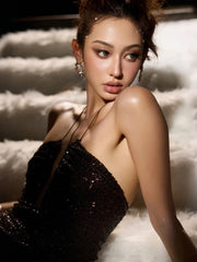 Woman in a black sequined dress sitting on a textured white surface