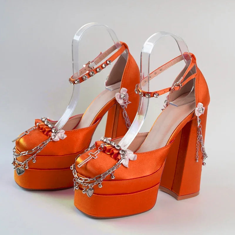 Orange high-heeled shoes with clear straps and decorative elements on a light gray background