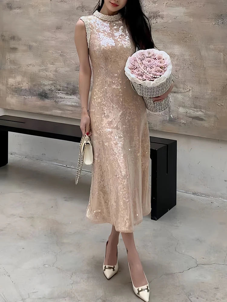 Woman in a beige sequin dress holding a bouquet of pink roses in an indoor setting.
