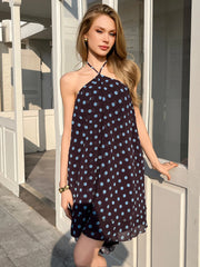 Woman wearing a polka dot dress standing on a sunlit porch.