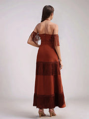 Woman wearing a rust-colored off-shoulder dress with fringe details on a plain background