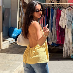 Woman in a yellow top and sunglasses standing in front of a clothing stall.