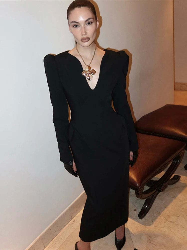 Woman in a black dress standing indoors with a neutral background
