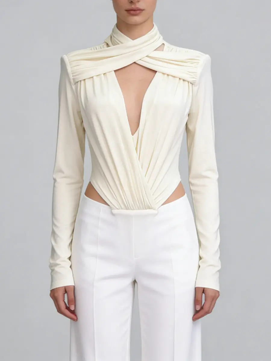 An apricot long-sleeve top with a deep neckline and pleated design, paired with white pants on a grey background.