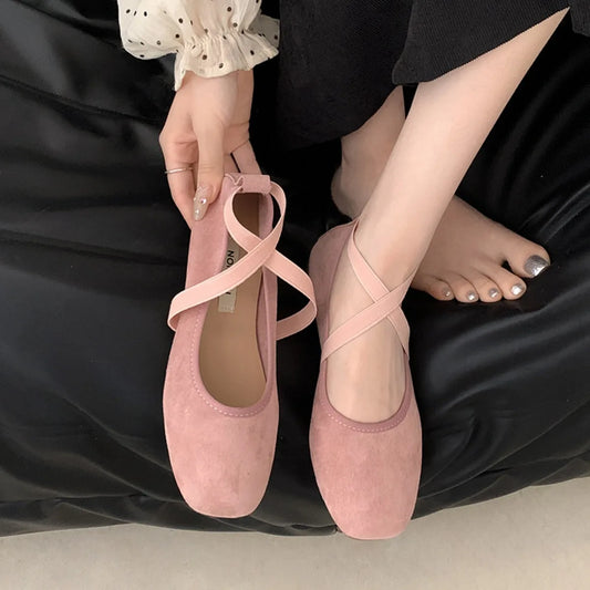 Square toe ballet flats with pink criss-cross straps on a black background