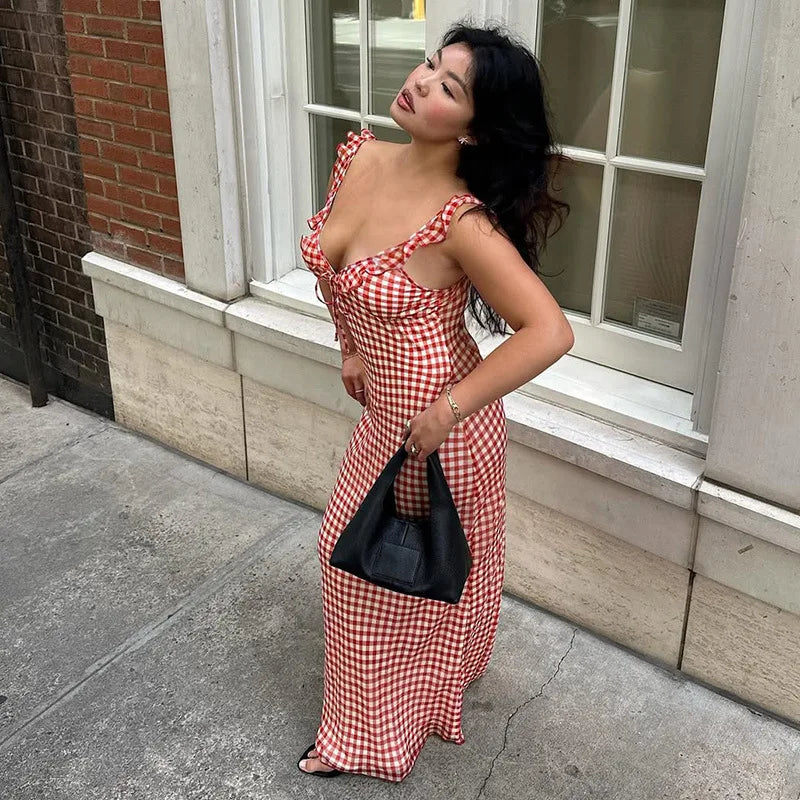 Woman in a red and white checkered dress standing on a sidewalk.