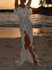 Woman in a white lace dress standing on a beach at sunset.