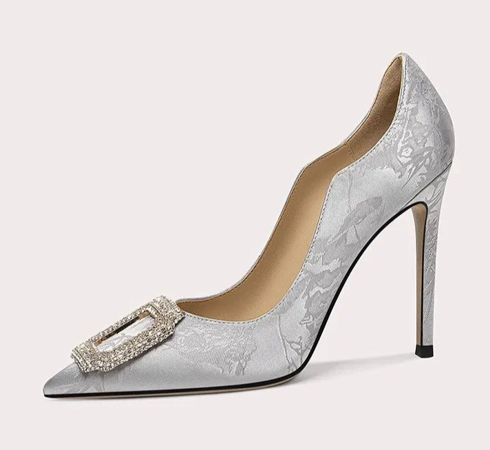 Silver high-heeled shoe with decorative buckle on a white background