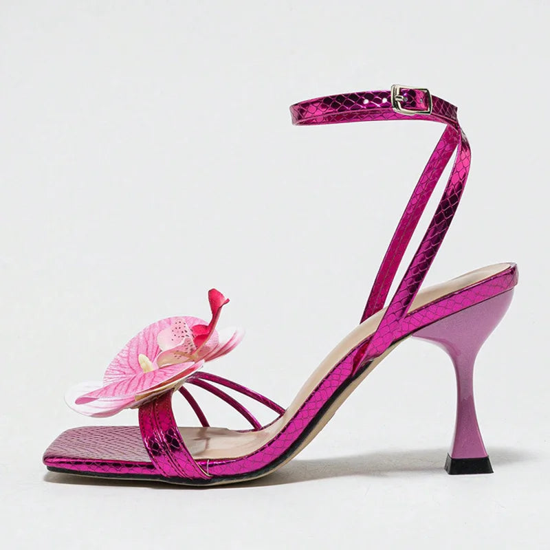 Pink high-heeled sandal with a decorative flower on a light gray background