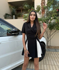 Woman in a black dress standing next to a white car with plants in the background