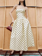 Woman wearing a strapless polka dot dress against a wooden paneled wall.