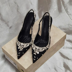 Black pointed toe slingback pumps with crystal embellishments on a shoebox