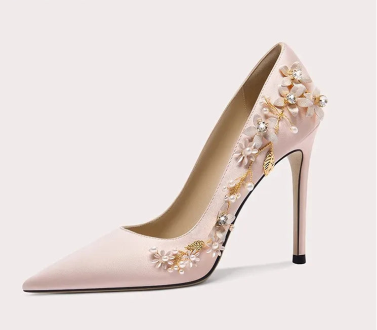 Pink high-heeled shoe with floral embellishments on a light gray background