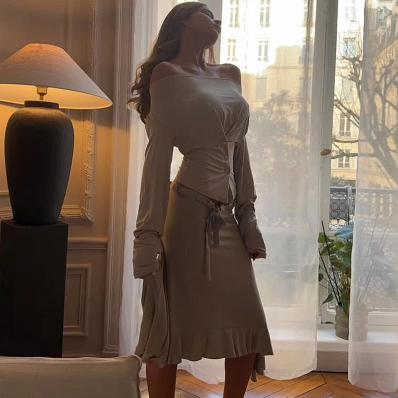 A woman in a beige top is standing in a room with a lamp and a large window.