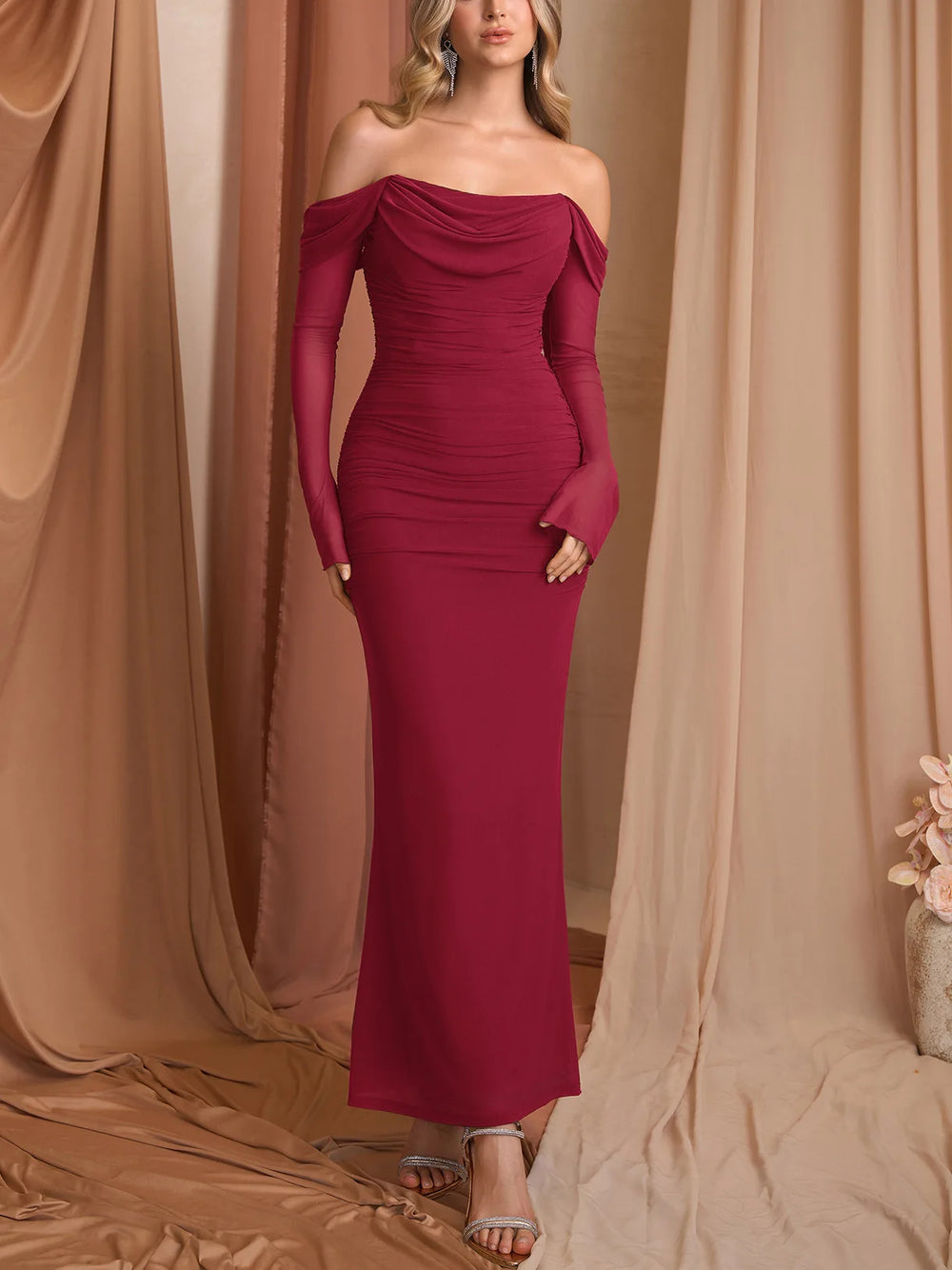 Woman wearing a burgundy off-shoulder gown against a beige curtain backdrop