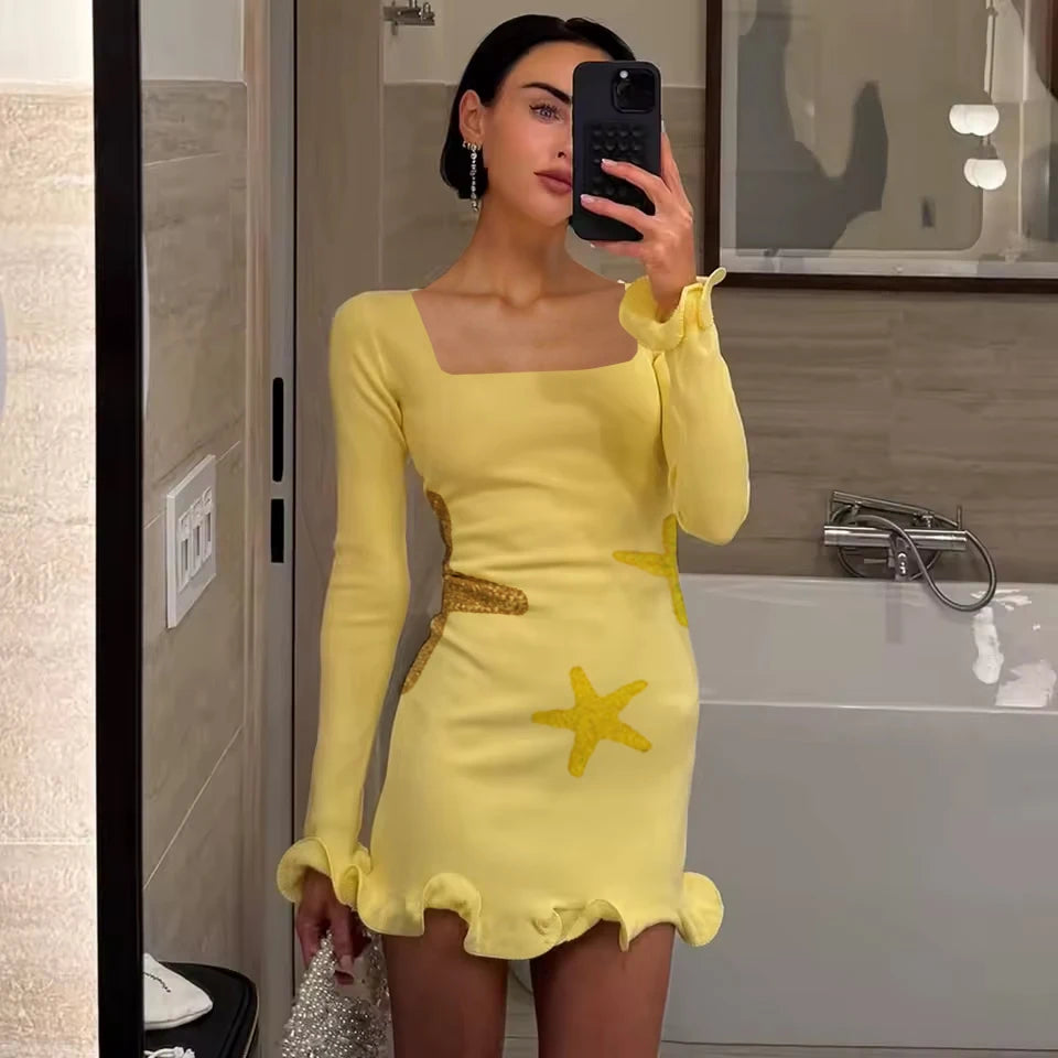 Woman taking a mirror selfie wearing a yellow dress with starfish designs in a bathroom.