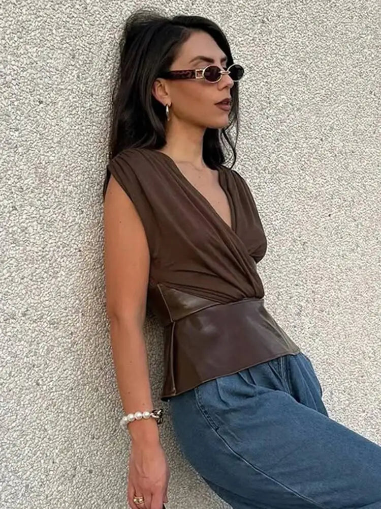 Woman wearing a brown sleeveless top and blue jeans against a textured wall.