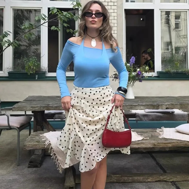 Woman in a blue top and polka dot skirt holding a red purse outdoors.