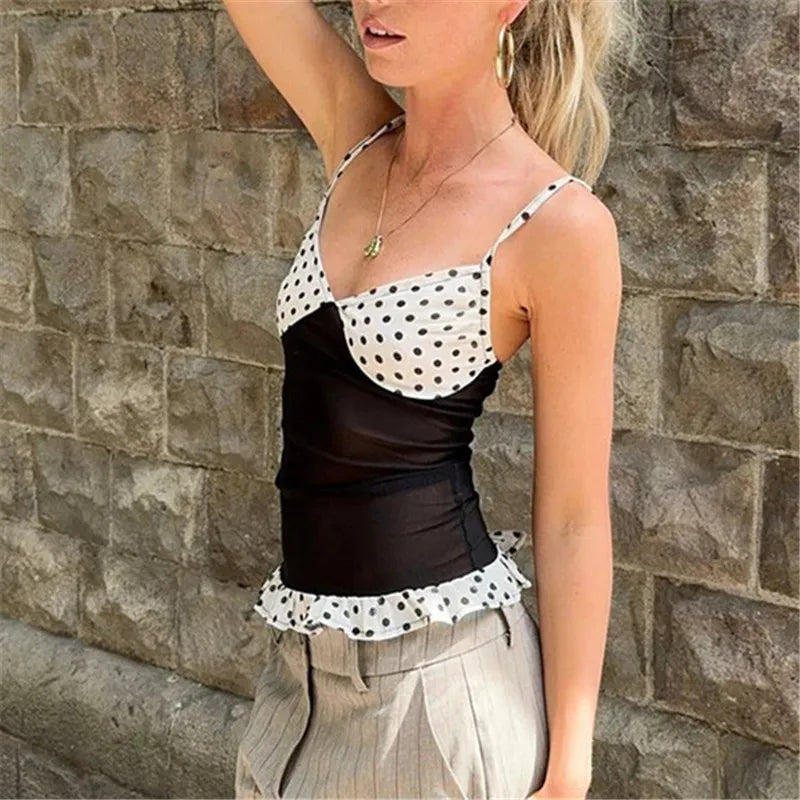 Woman wearing a polka dot top and beige pants against a stone wall.