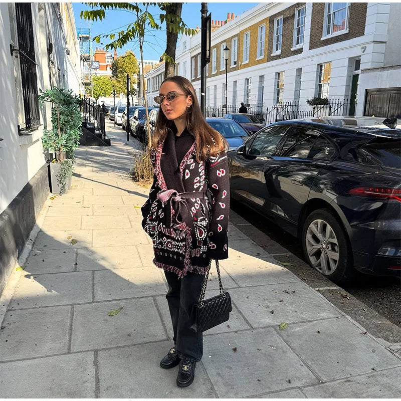 Woman walking on a street wearing a patterned coat and sunglasses.