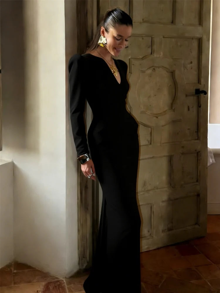 Woman in a black dress standing against a textured wall.