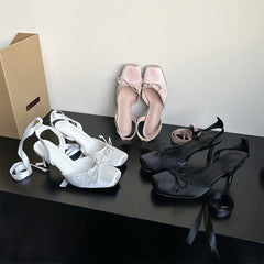 Three pairs of women's shoes (white, pink, black) on a dark surface with a cardboard box.