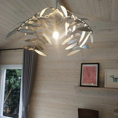 A dramatic iron palm leaf chandelier hanging in a modern dining room with natural light streaming in. E