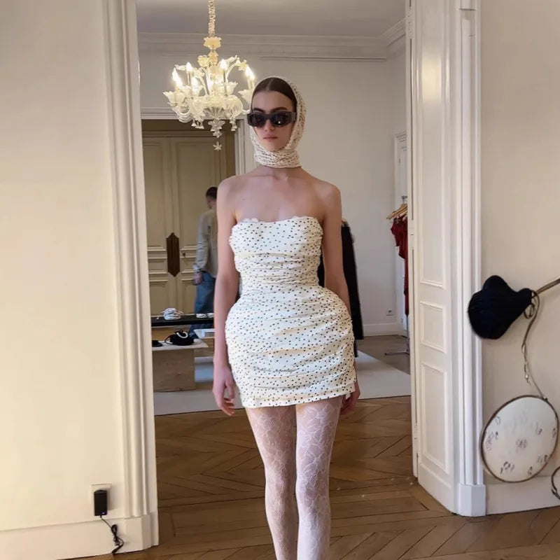 Woman in a strapless white dress standing in a room with a chandelier.