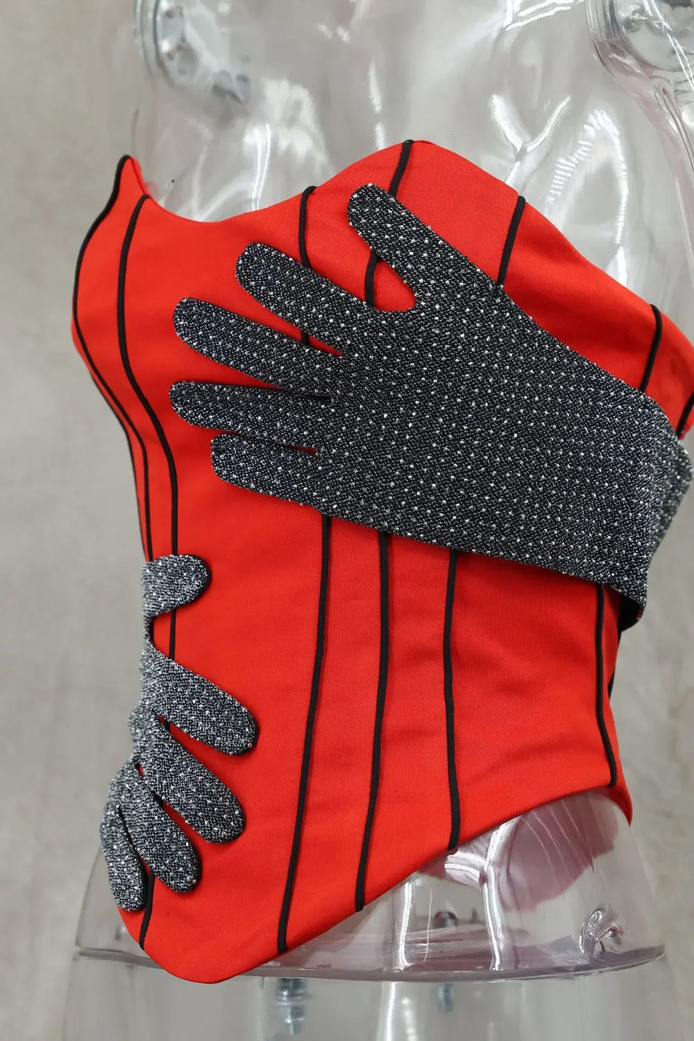 Red and black striped glove with textured gray palm on a clear mannequin arm.