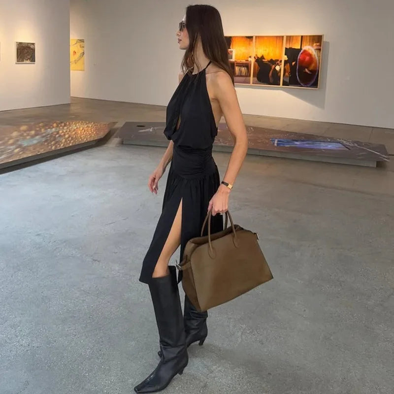 Woman in a black dress and boots holding a brown bag in an art gallery.