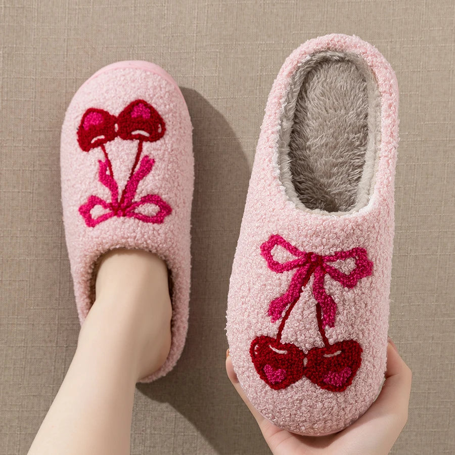 Foot wearing a pink plush slipper with cherry bow