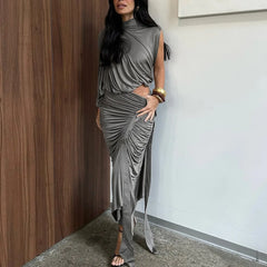 Woman wearing a gray draped dress standing against a wooden wall.