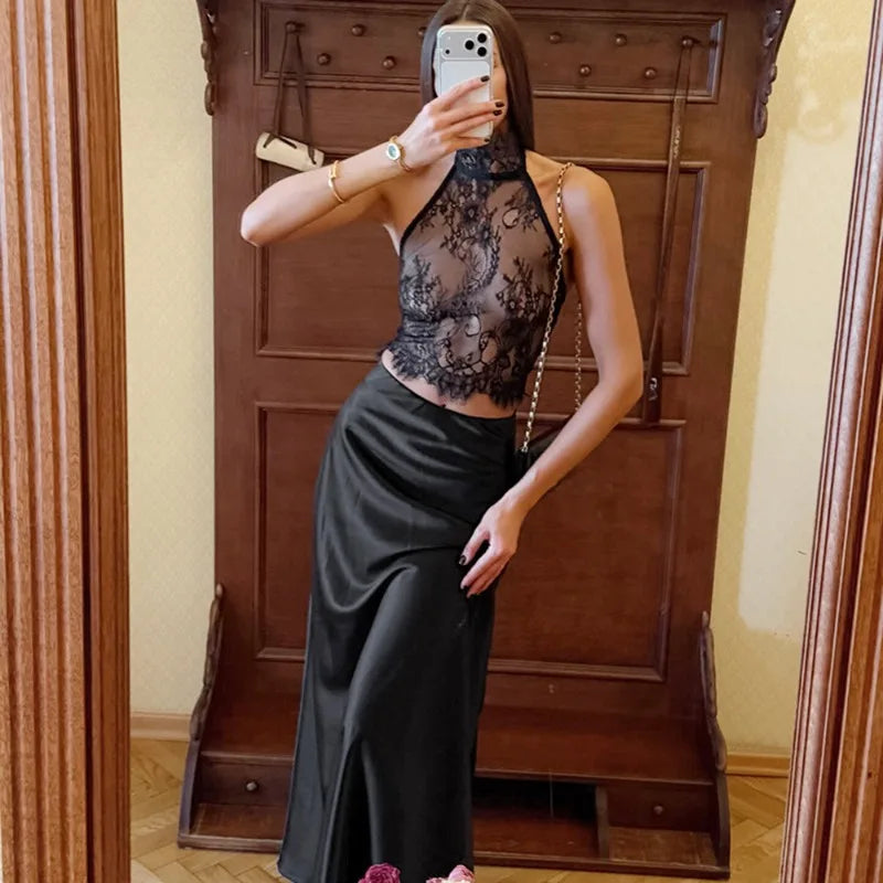 Person wearing a black lace top and black skirt in front of a wooden door.