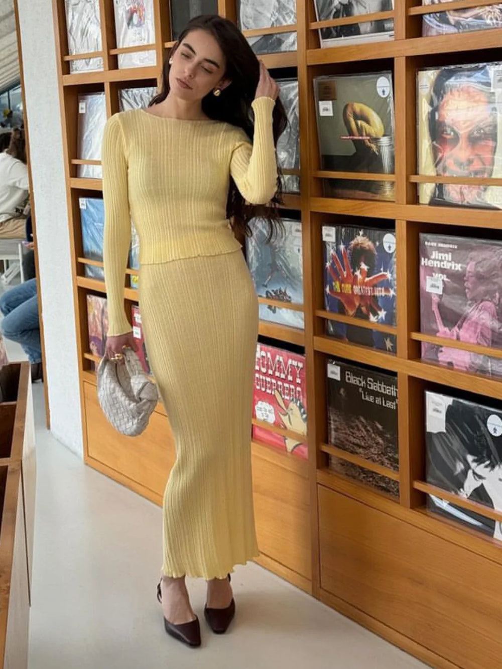 Woman in a yellow dress standing in front of a bookshelf with records