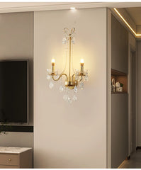 A luxurious crystal wall sconce with a gold finish, illuminating a modern living room. Golden Atelier 11