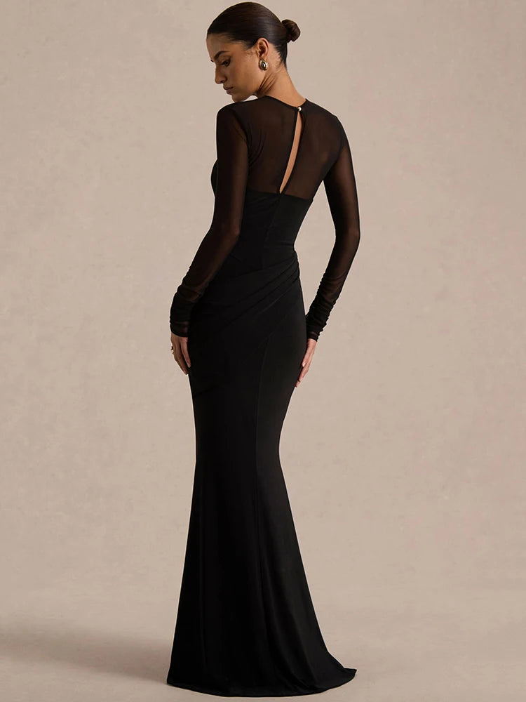 Woman wearing a black evening gown with sheer sleeves against a beige background