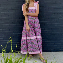 Woman wearing a pink floral dress against a black brick wall.