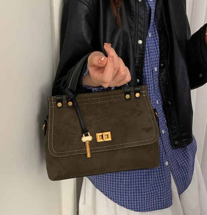 Person holding a brown leather handbag with a gold clasp against a neutral background
