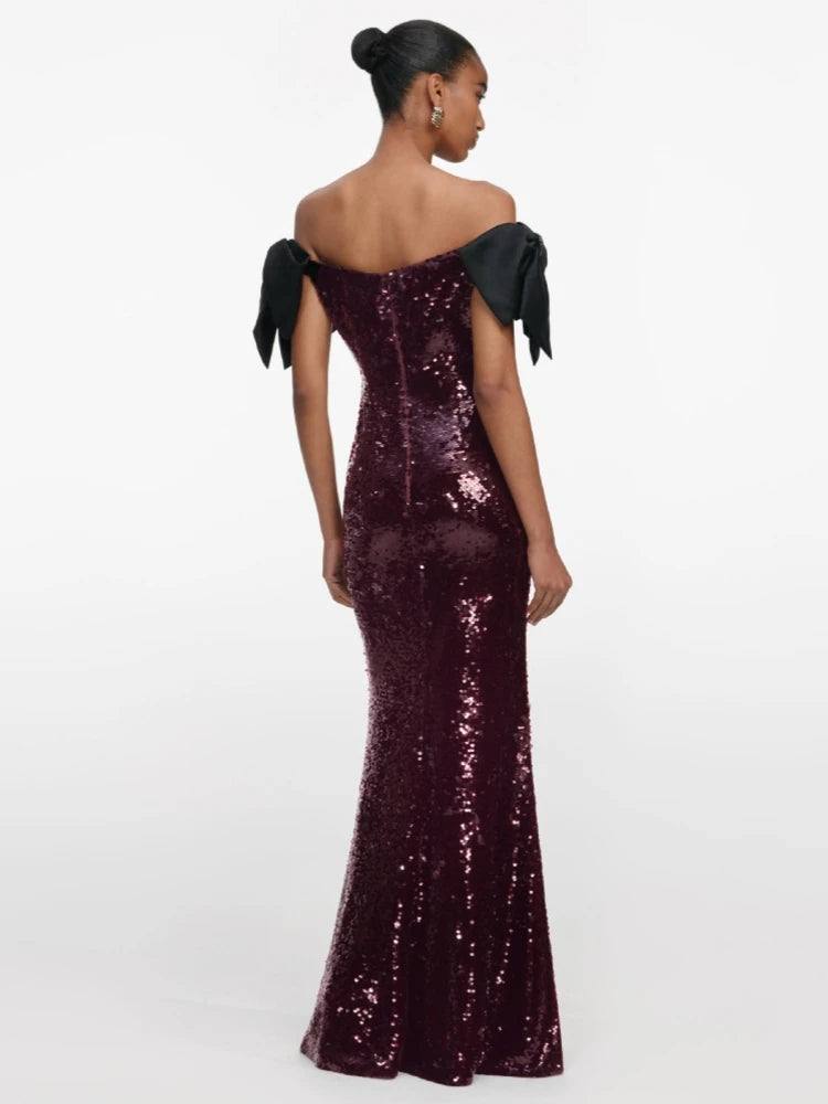 Woman wearing a burgundy sequin gown with black bow straps on a white background
