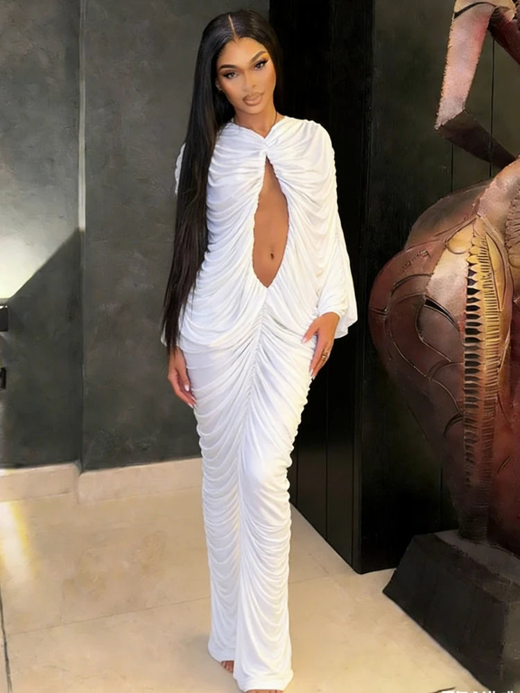 Woman in a white draped gown standing in a room with dark walls and a large sculpture.