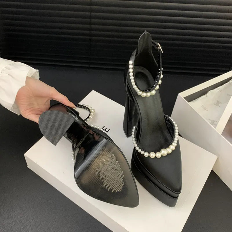 Black high-heeled shoes with pearl detailing on a black surface