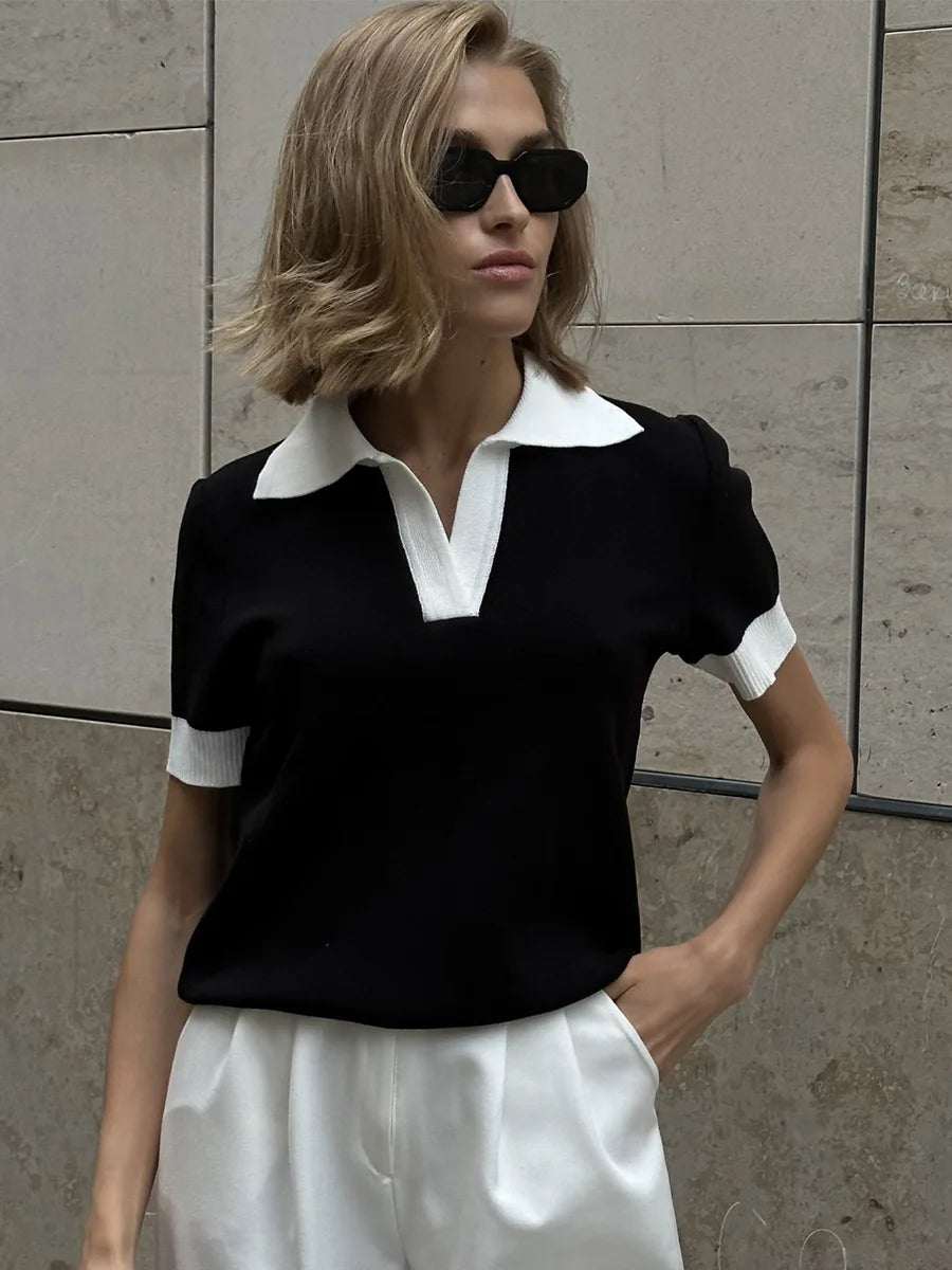 Woman wearing a black and white outfit with sunglasses against a stone wall.