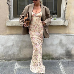 Woman wearing a floral dress and beige coat standing against a wall.