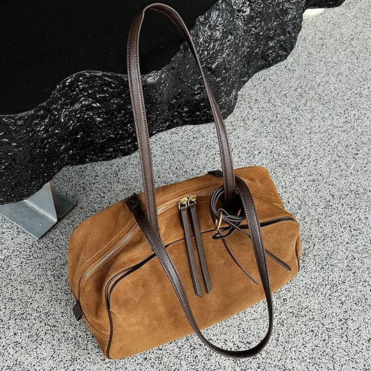Brown suede handbag with a strap on a textured surface