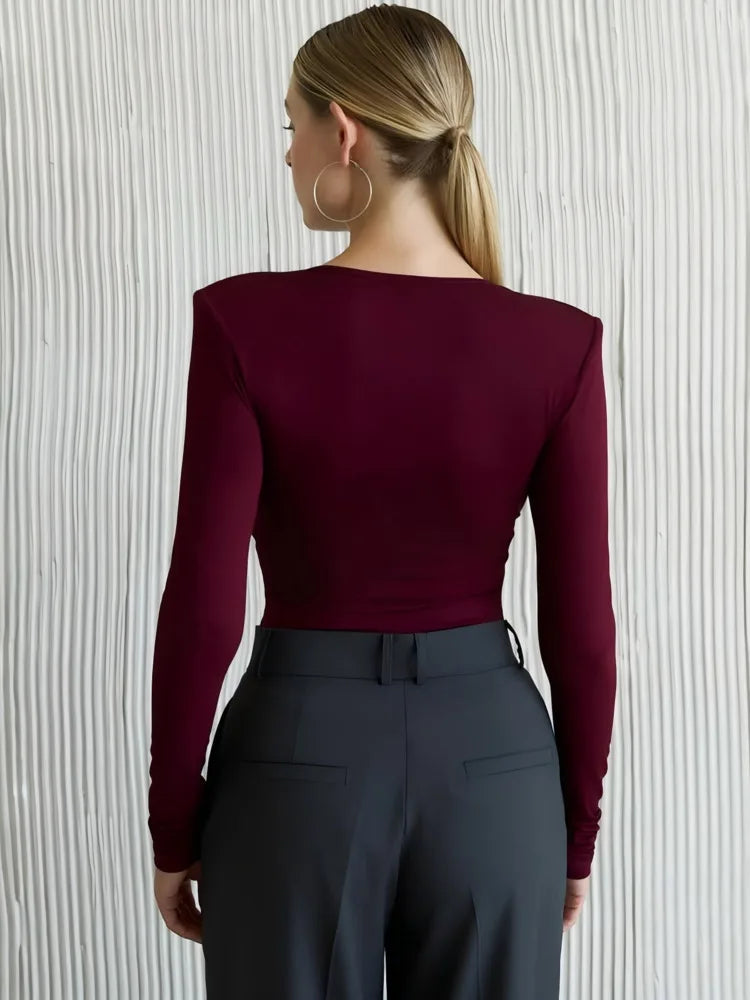 Person wearing a burgundy long-sleeve top and dark pants against a neutral background