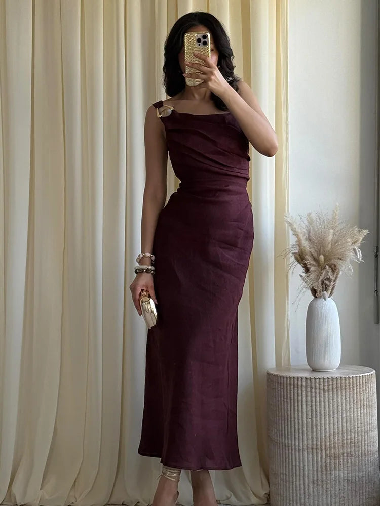 Woman in a burgundy dress taking a mirror selfie against beige curtains.